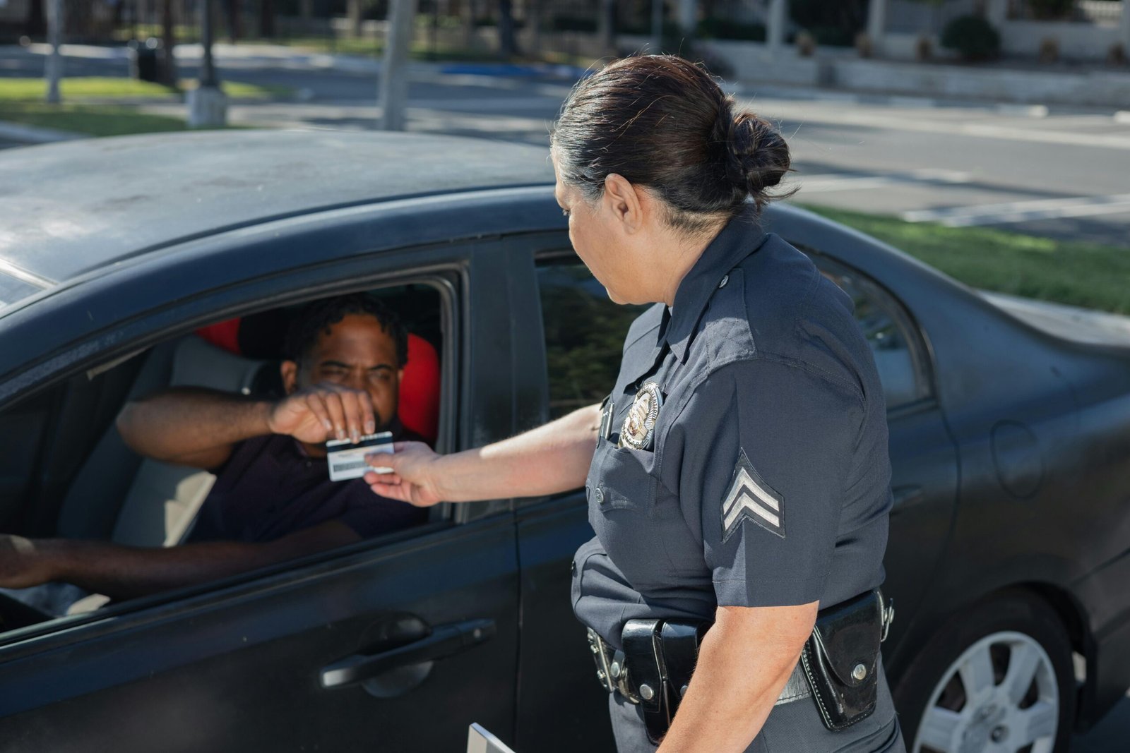 A police officer hands a ticket to a driver in a car on a sunny day street.